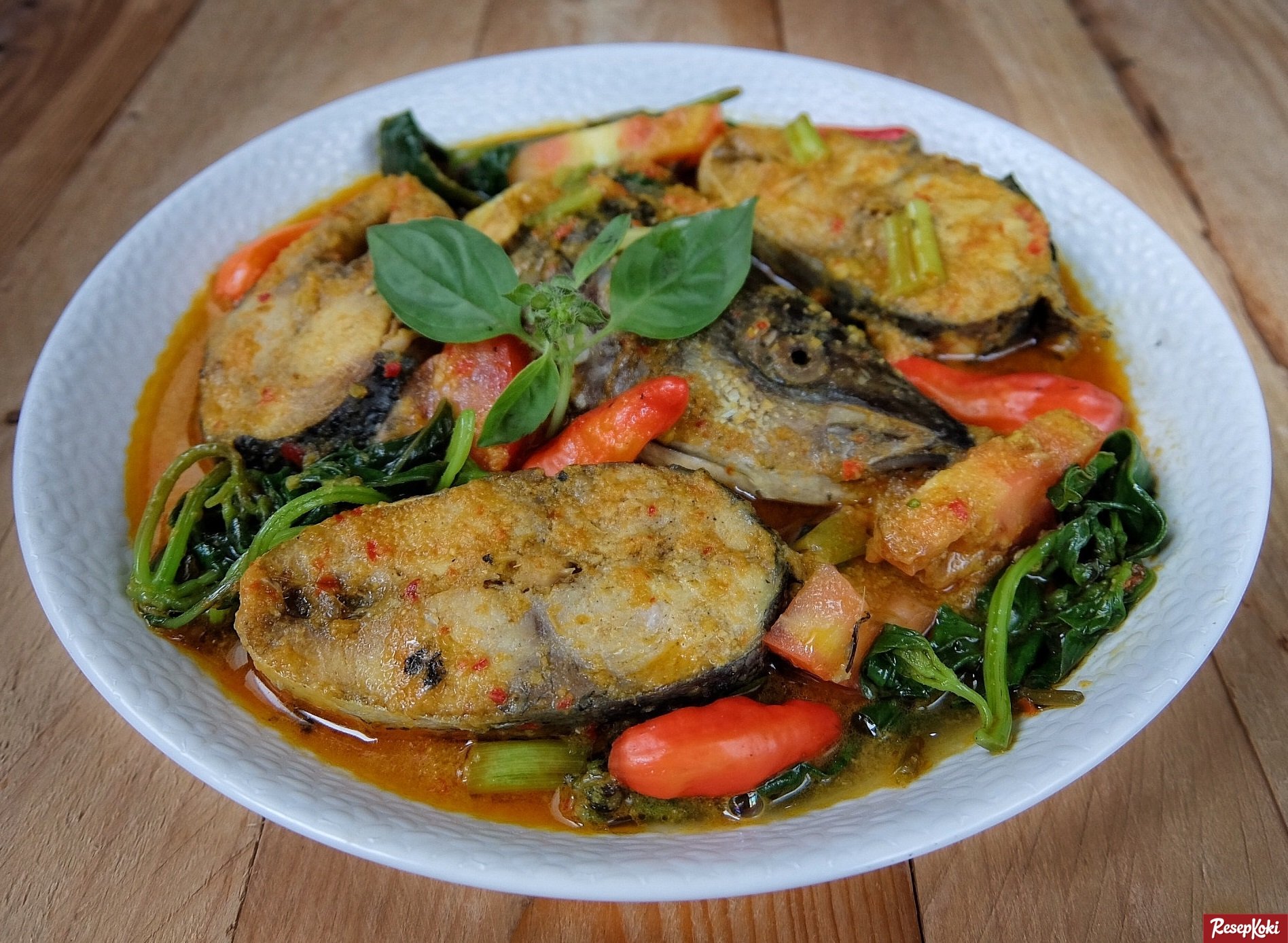 Proses memasak Ikan Woku Belanga di atas kompor tradisional